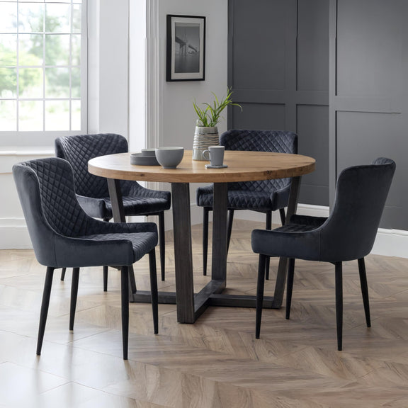 Dining room with a round wooden table and six dark chairs on a wooden floor.