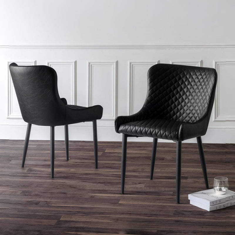 Two black chairs on a wooden floor with a white paneled wall in the background.