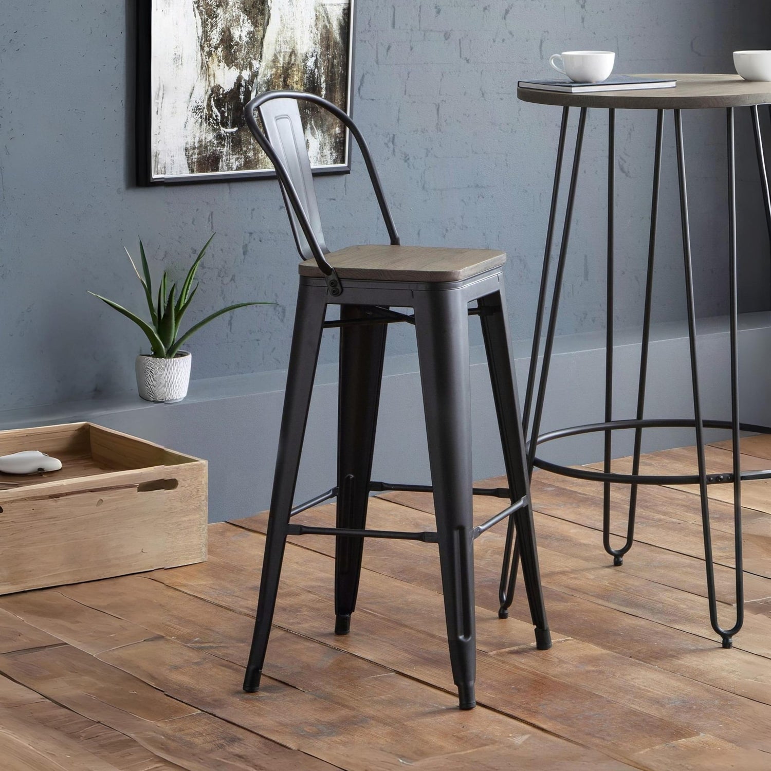 Bar stool with wooden seat and black metal frame in a room with a plant and wooden box.