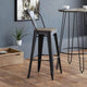 Bar stool with wooden seat and black metal frame in a room with a plant and wooden box.