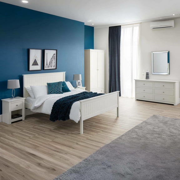 Modern bedroom with blue accent wall, white furniture, and wooden floor.