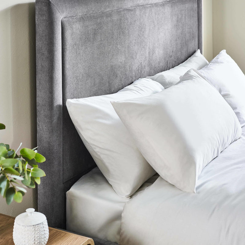 Gray upholstered headboard with white pillows on a bed in a bedroom setting.