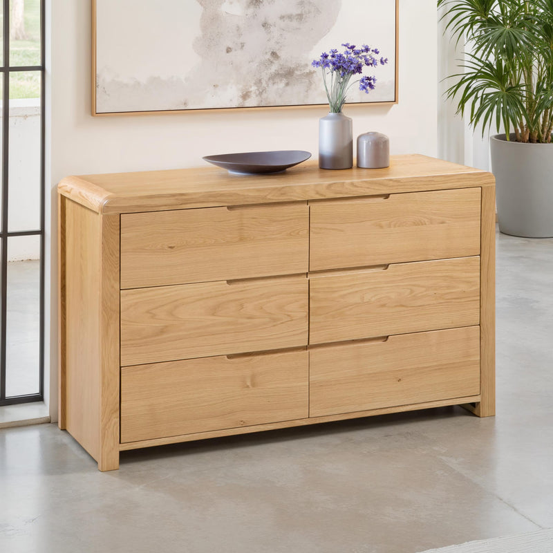 Wooden dresser with decorative items in a room with a plant and framed artwork.