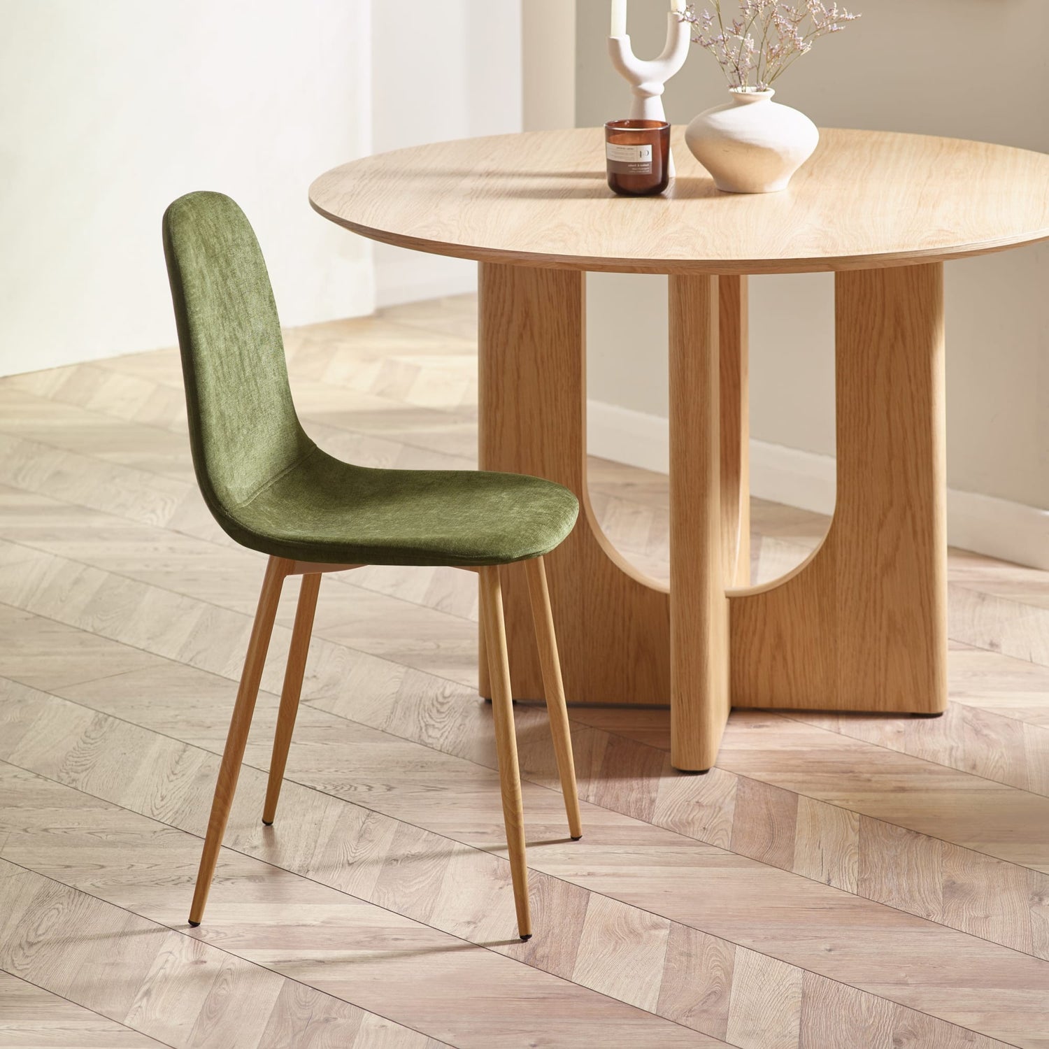 Green chair in front of a wooden dining table on a wooden floor.