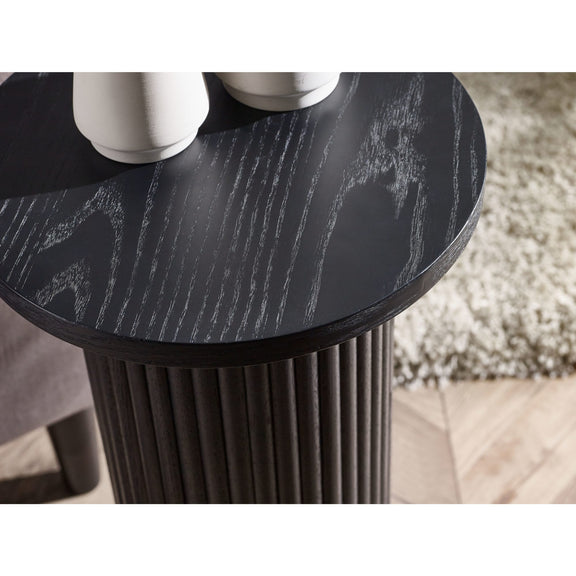 Round black marble table with cylindrical base on a light wood floor.