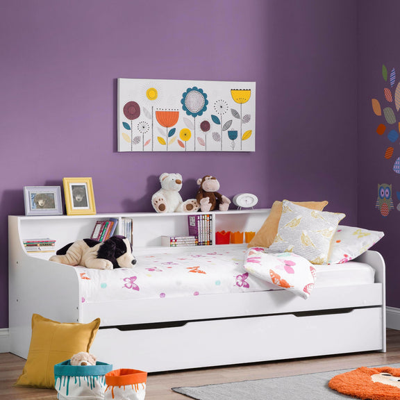 Children's room with a white bed, colorful pillows, and toys against a purple wall.