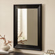 Black-framed mirror on a beige wall with decorative items below.