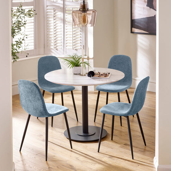 Round dining table with four blue chairs in a bright room with large windows.