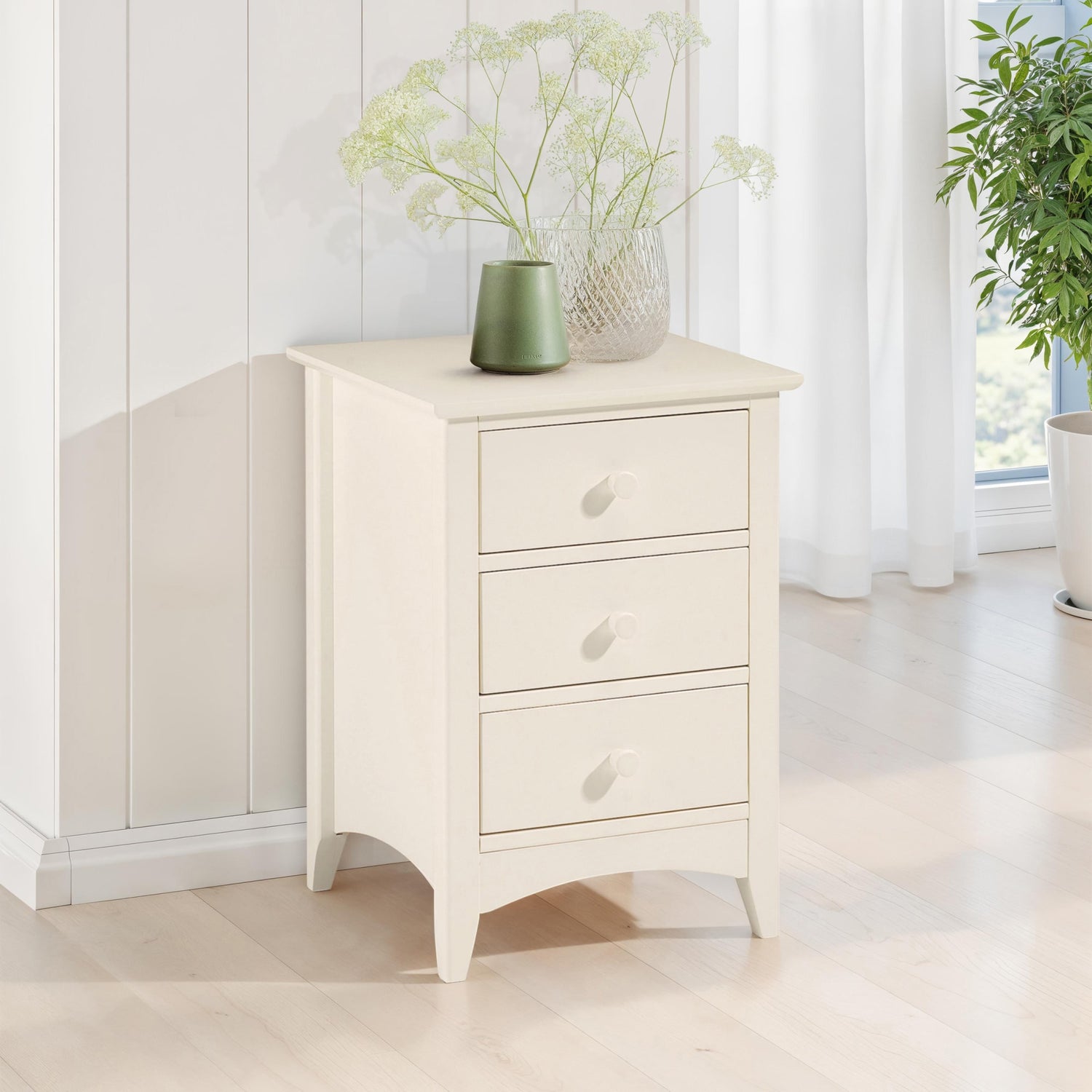 White nightstand with three drawers in a bright room with plants