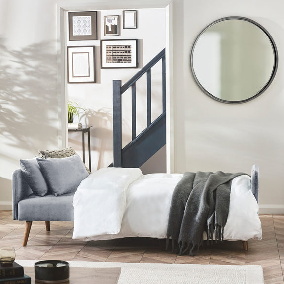 Modern bedroom with a bed, armchair, and round mirror.