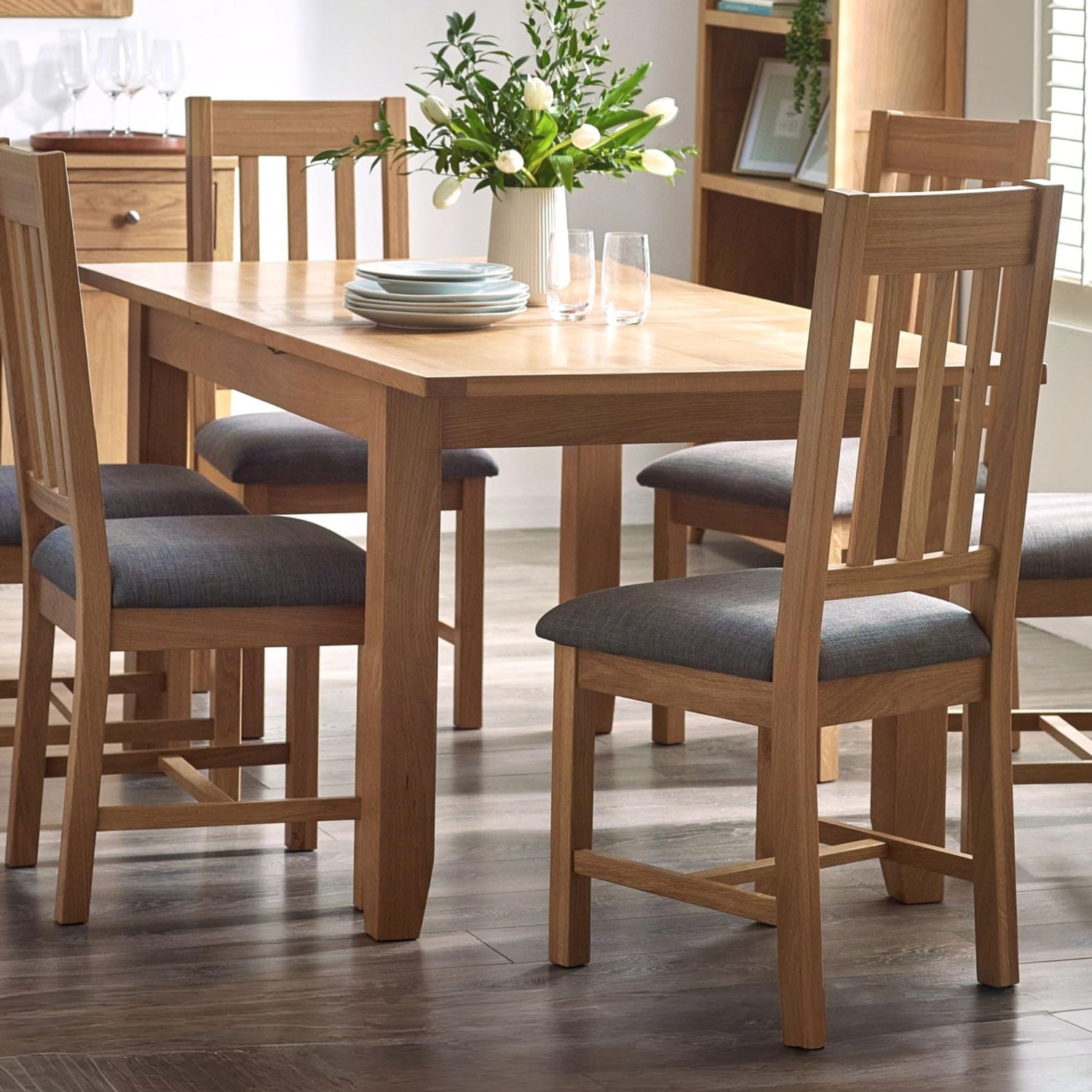 Wooden dining table with chairs and a vase of flowers in a room.