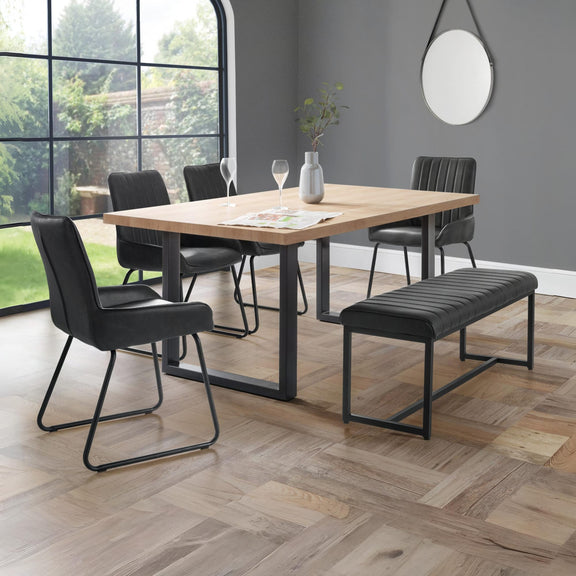 Dining area with wooden table, black chairs, and bench in a room with large windows.