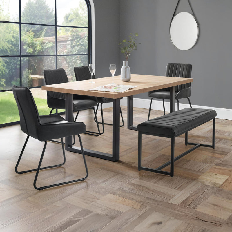 Dining area with wooden table, black chairs, and bench in a room with large windows.