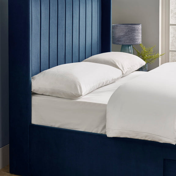 Bed with white bedding and pillows against a blue headboard.