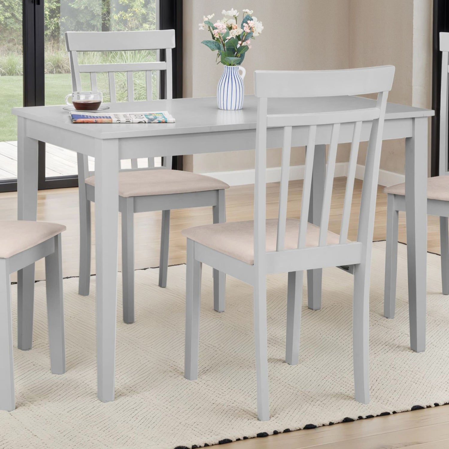 Gray dining table with four chairs in a room with a window and rug.
