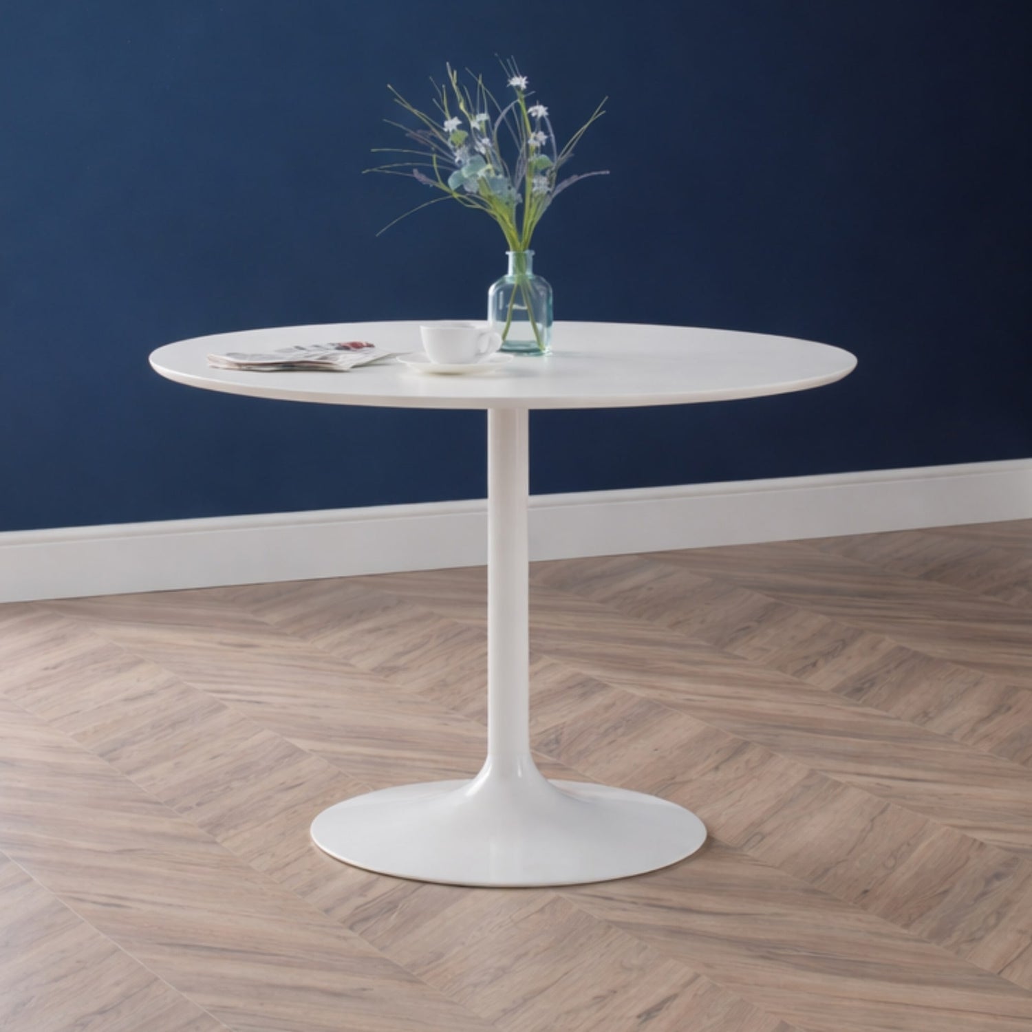 Round white table with a vase of flowers against a blue wall.