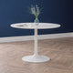 Round white table with a vase of flowers against a blue wall.