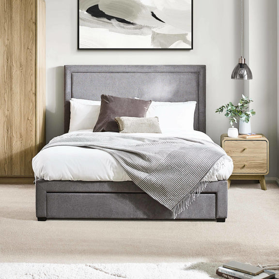 Gray upholstered bed in a bedroom setting with a side table and abstract art on the wall.