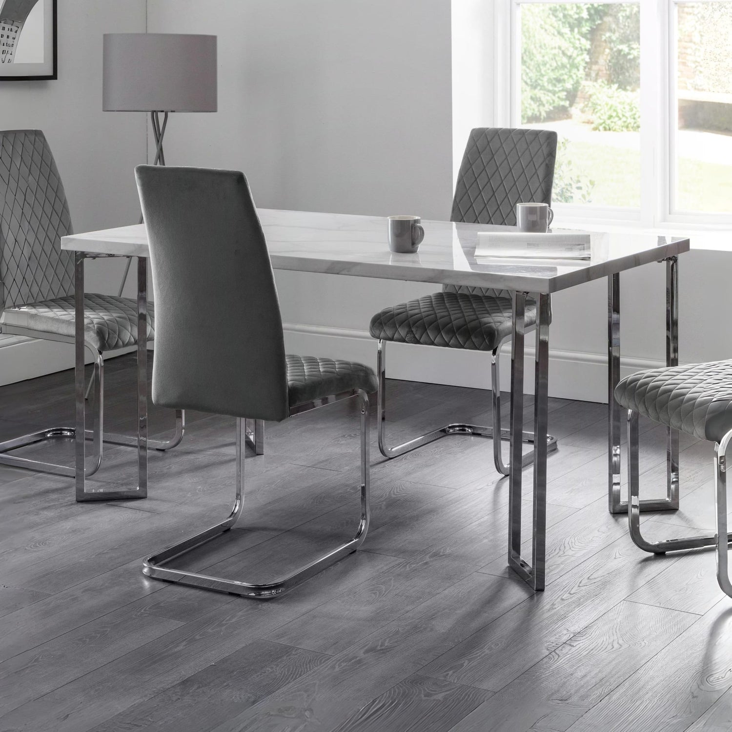 Modern dining room with a glass table and gray chairs on a wooden floor.