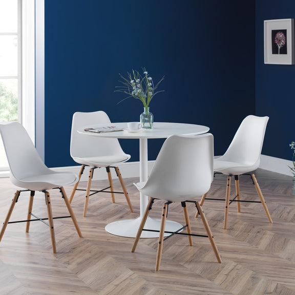 Dining area with a round table and white chairs against a blue wall.