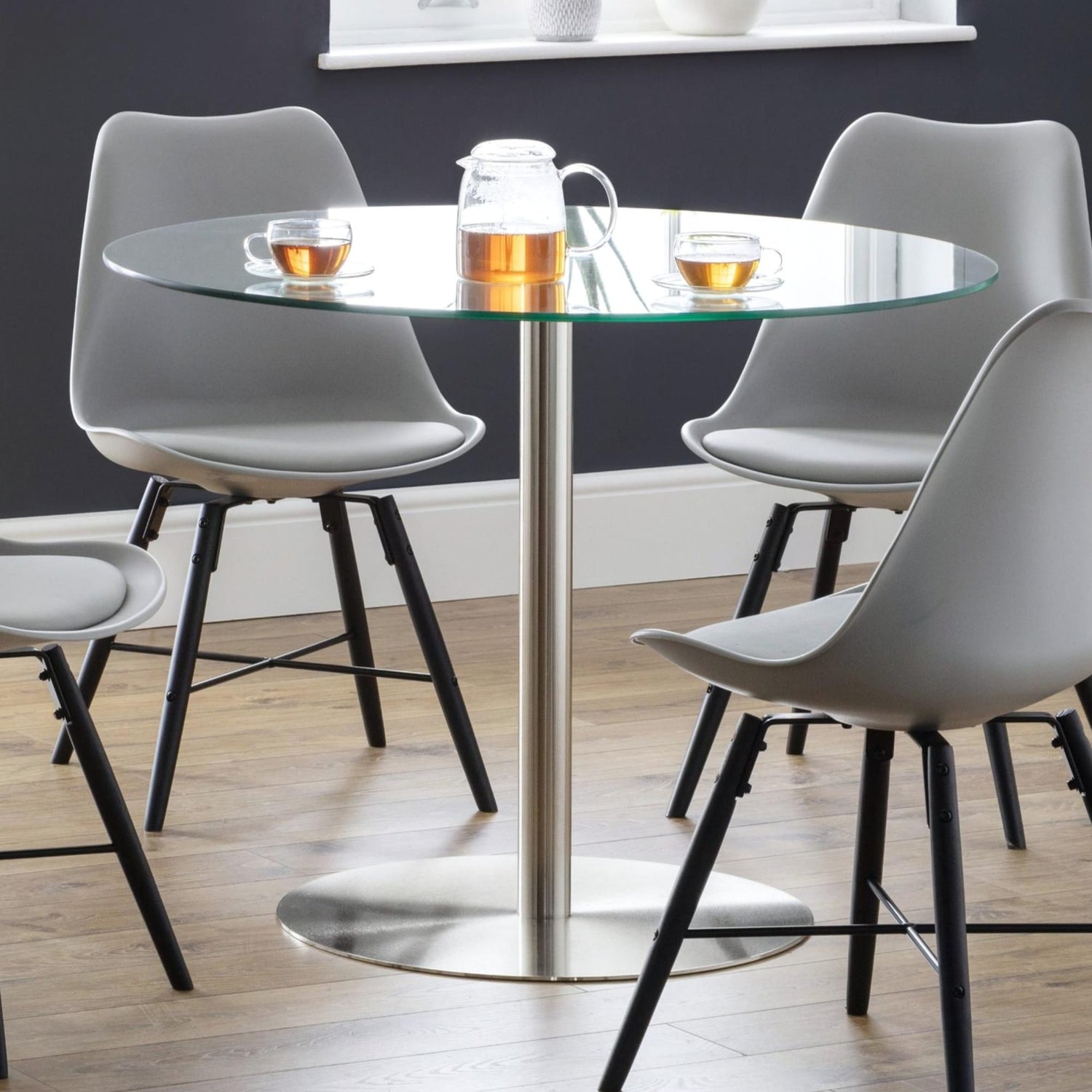 Round glass dining table with four gray chairs in a modern setting.
