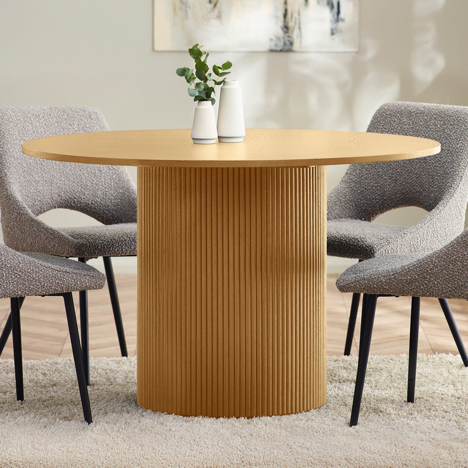 Round wooden dining table with textured base in a room setting with chairs and decor.