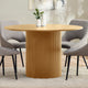 Round wooden dining table with textured base in a room setting with chairs and decor.