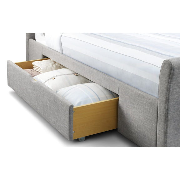Gray upholstered bed with an open drawer containing folded white bedding on a white background