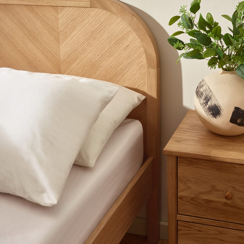 Wooden bed with white pillows and a nightstand with a plant