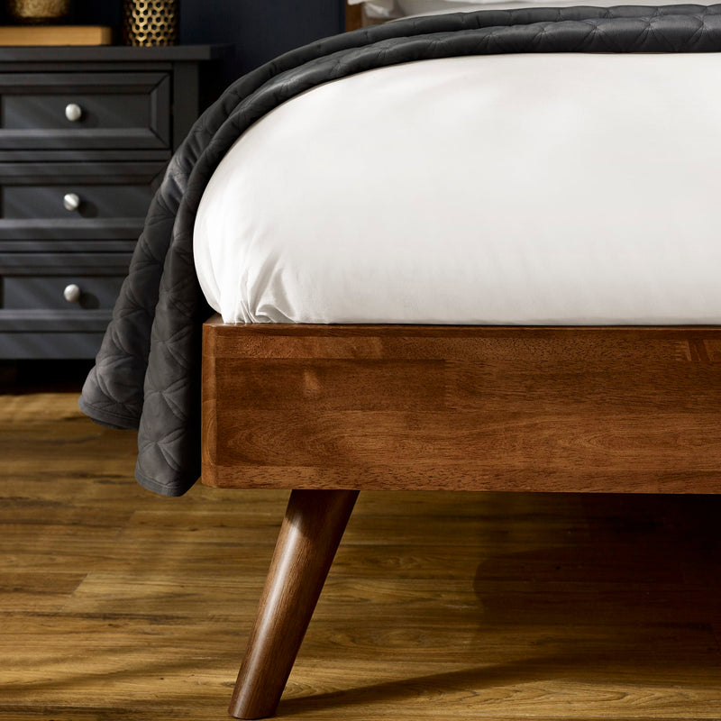 Wooden bed frame with a white mattress and gray blanket in a bedroom setting.