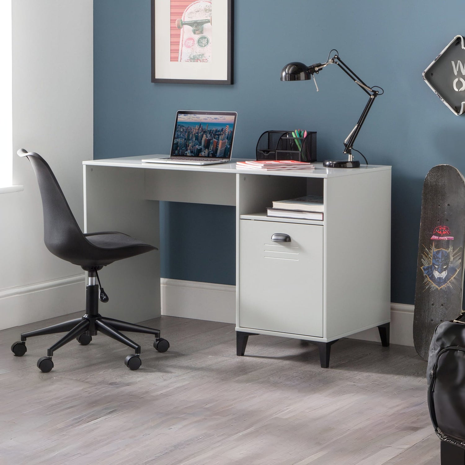 White desk with a laptop, lamp, and office supplies against a blue wall.
