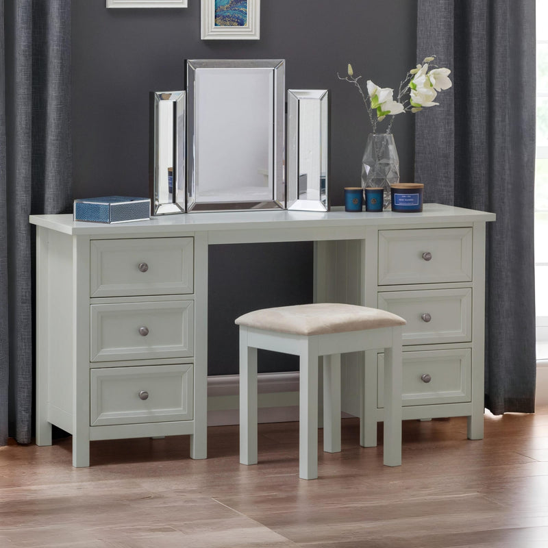 White dressing table with mirrors, stool, and decorative items against a gray wall.