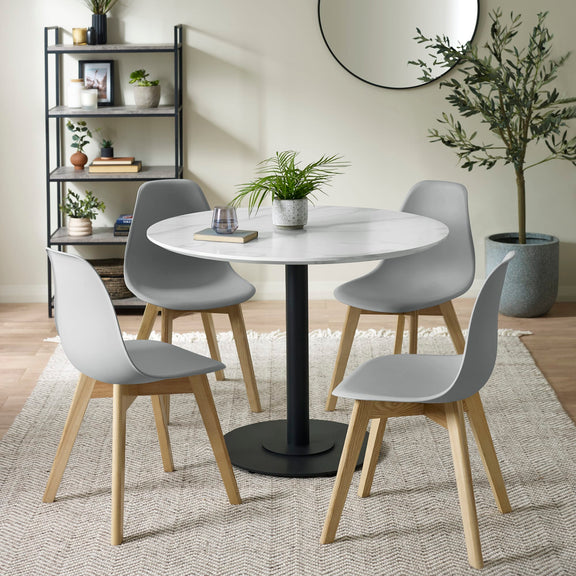 Dining room with a round table and four chairs, plants, and a bookshelf.
