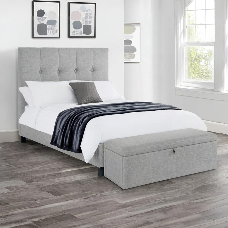 Gray upholstered bed with white bedding and a gray ottoman in a room with framed art on the wall.