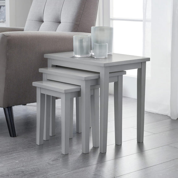 Set of three gray nesting tables with glass candle holders in a living room setting.