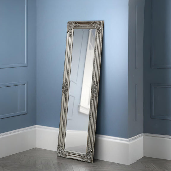 Decorative floor mirror with an ornate frame against a blue wall.