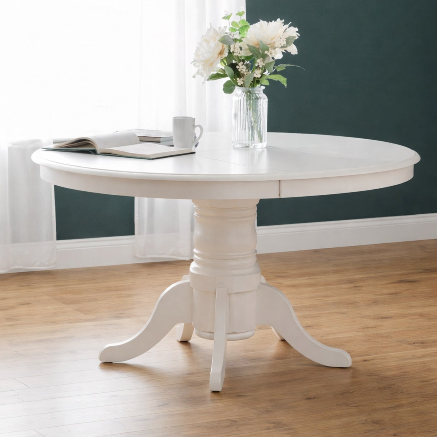 White round dining table with a vase of flowers in a room with a dark green wall.