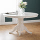 White round dining table with a vase of flowers in a room with a dark green wall.
