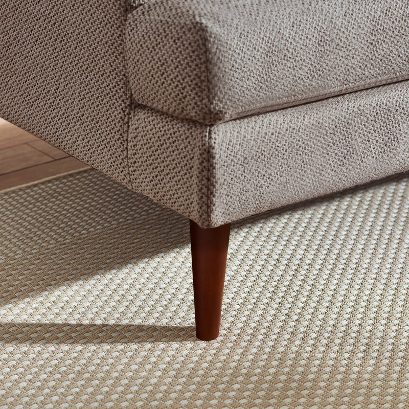 Close-up of a textured sofa corner with wooden leg on a patterned carpet