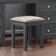 Gray stool with beige cushion in front of a gray dresser.