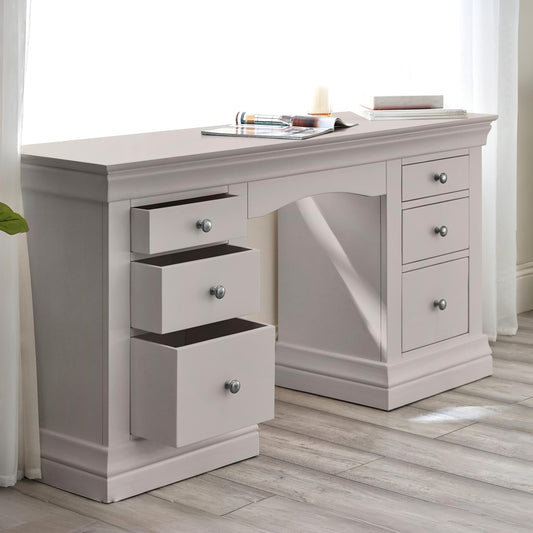 Gray desk with multiple drawers in a room with light wood flooring and white curtains.