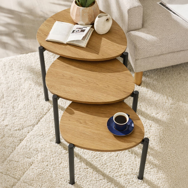 Stack of wooden side tables with a cup and saucer on a carpeted floor.