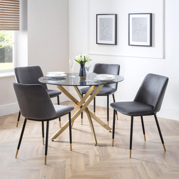 Dining room with a round glass table and four gray chairs on a wooden floor.