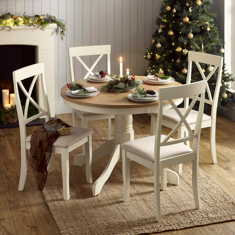 Dining room with a round wooden table and white chairs, decorated for Christmas.