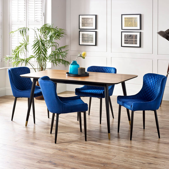 Dining room with a wooden table and blue chairs, featuring a plant and framed pictures on the wall.