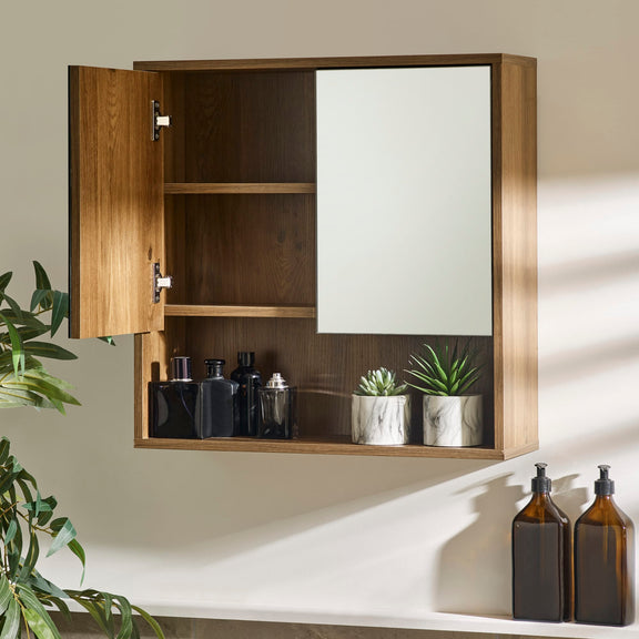 Wooden wall-mounted cabinet with open door displaying bottles and plants, on a neutral background.