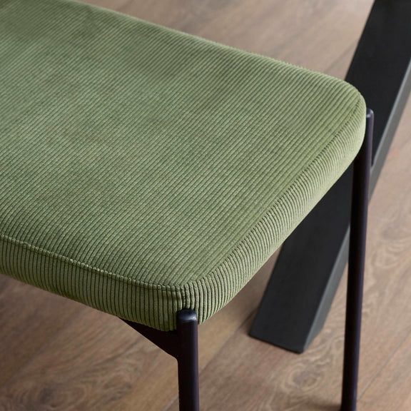 Green cushioned stool with black metal legs on a wooden floor