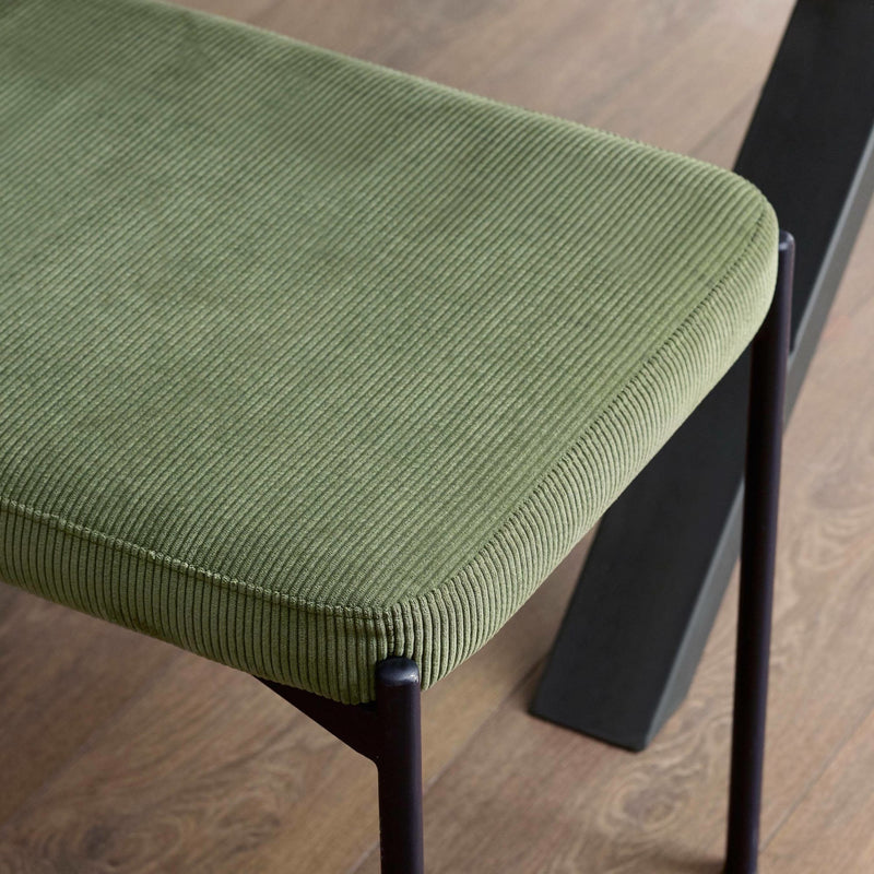 Green cushioned stool with black metal legs on a wooden floor