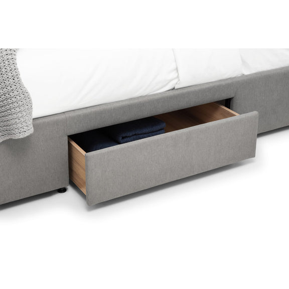 Gray upholstered bed with an open drawer revealing a blue garment on a white background