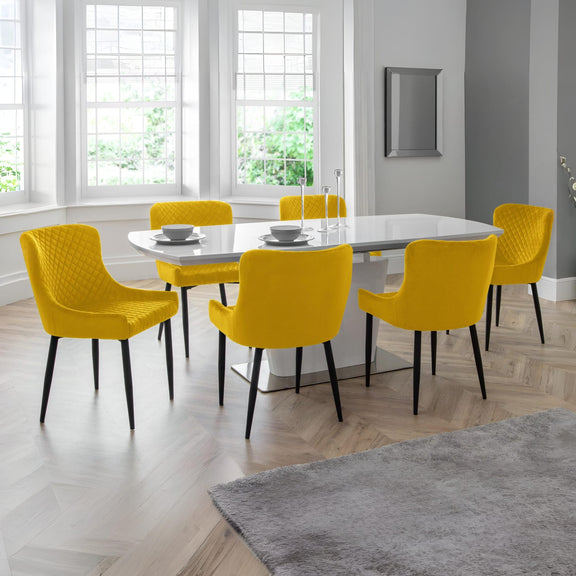 Dining room with a white table and yellow chairs near large windows.